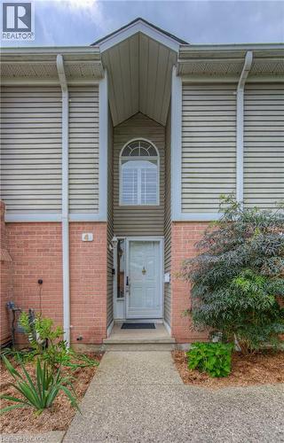 Front entry featuring a white door with sidelight, brick and siding exterior, arched window with shutters, concrete walkway, and landscaping