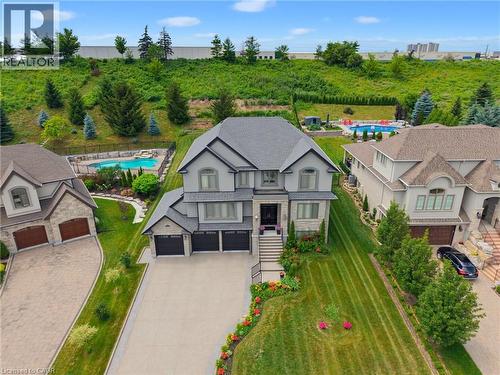 Grand two-story residence featuring a gray exterior with stone accents, a multi-car garage, expansive driveway, and meticulously landscaped front garden beds