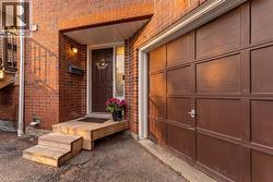Brick exterior with an attached garage featuring a panel door, wooden steps leading to the main entrance, and an outdoor wall light fixture