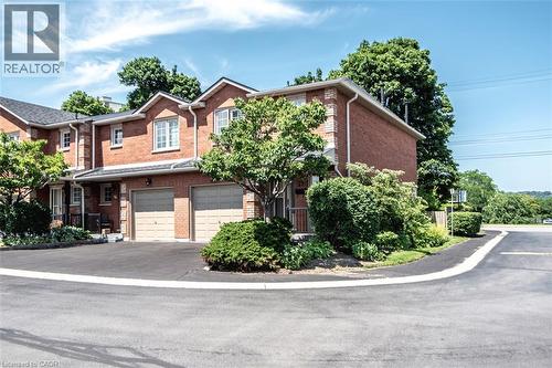 Red brick exterior featuring white-framed windows, individual garage doors, and a paved driveway