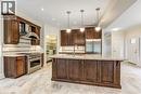 Gourmet kitchen featuring a large central island with integrated wine rack, Monogram stainless steel appliances, dark wood cabinetry built by Barzotti cabinetry  and pendant lighting