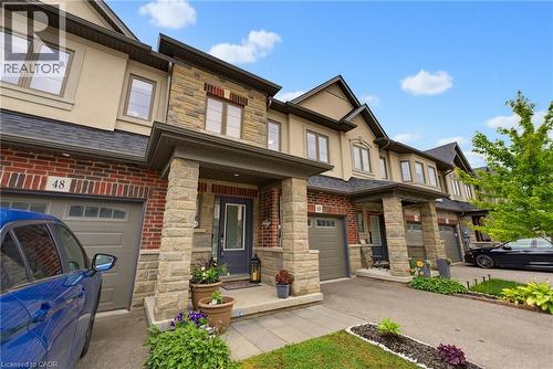 Contemporary townhome facade featuring brick and stone masonry, single-car garage with a panel door, covered front entry, and multiple windows with dark trim