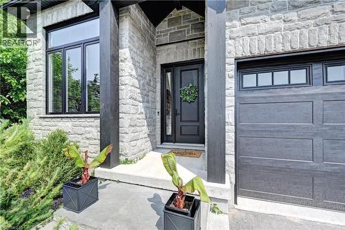 Stone facade entrance featuring a dark wood-paneled door with transom window, modern black-framed windows, and an integrated garage with upper window panels