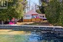 Pink-sided property with a waterfront setting featuring a wood deck, glass panel railing, and a stone retaining wall
