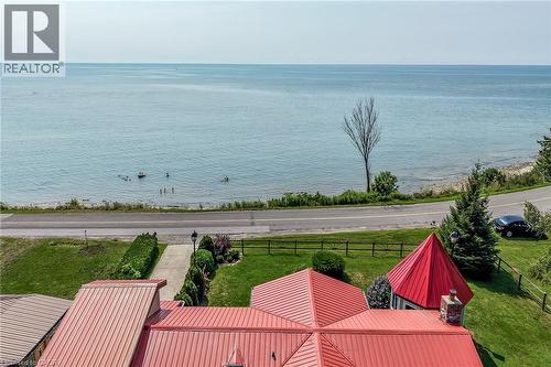 Waterfront property featuring manicured grounds with mature landscaping, a red metal-roof pavilion structure, and direct access to a private sandy beach