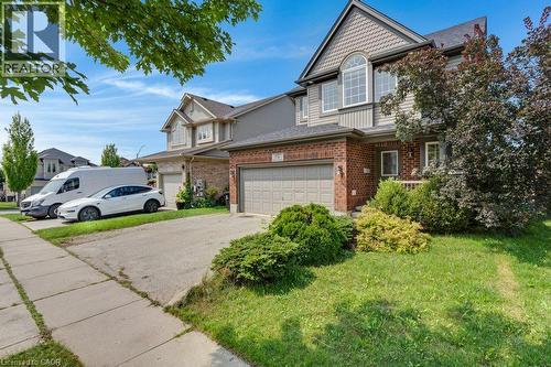 Brick and siding exterior with an integrated garage, arched window, and mature landscaping