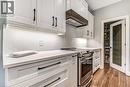 White shaker cabinetry with matte black hardware, under-cabinet lighting, stainless steel induction range, and a frosted 1-lite glass pantry door
