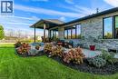 covered patio with fan, expansive windows, exposed aggregate concrete patio, and landscaped beds with mature shrubs