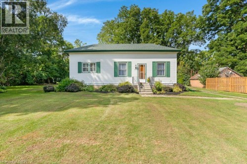 Classic cottage-style home featuring a clean white exterior with green shutters, a welcoming front entrance with steps and a covered porch, and mature landscaping with flowering shrubs