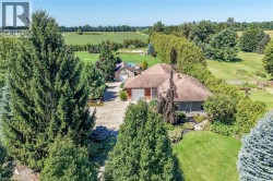 Expansive property featuring a single-story residence, detached garage, mature trees, manicured lawns, and a concrete driveway