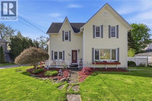 Yellow siding exterior with white trim, covered porch with white railing, established front landscaping, and a red front door