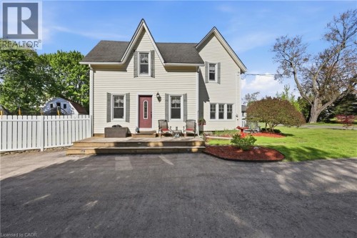 Two-story residence featuring light-colored siding, a prominent front deck, a white picket fence, and a spacious paved area
