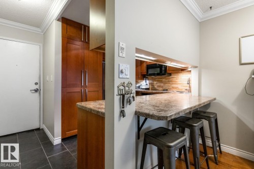 Kitchen with crown molding, a textured ceiling, a kitchen breakfast bar, tasteful backsplash, and brown cabinets