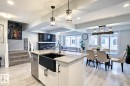 Kitchen featuring beam ceiling, white cabinets, pendant lighting, a stone fireplace, and a center island with sink
