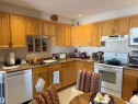 Kitchen featuring white appliances, a textured ceiling, under cabinet range hood, brown cabinets, and dark countertops