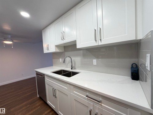 Kitchen with white cabinets, dishwasher, tasteful backsplash, light stone countertops, and dark wood-style floors
