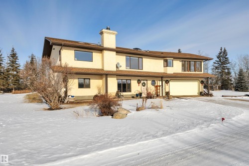 Snow covered house featuring an attached garage, stucco siding, and a chimney