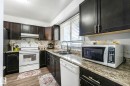 Kitchen with white appliances, light wood-type flooring, backsplash, light stone countertops, and dark cabinetry