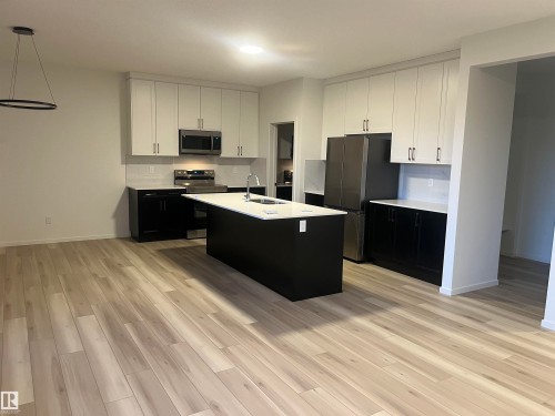 Dual tone kitchen with two tone cabinets, stainless steel appliances, light wood-style floors, a kitchen island with sink, and hanging light fixtures