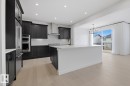 Kitchen featuring dark cabinets, a center island with sink, light wood-type flooring, tasteful backsplash, and hanging lights