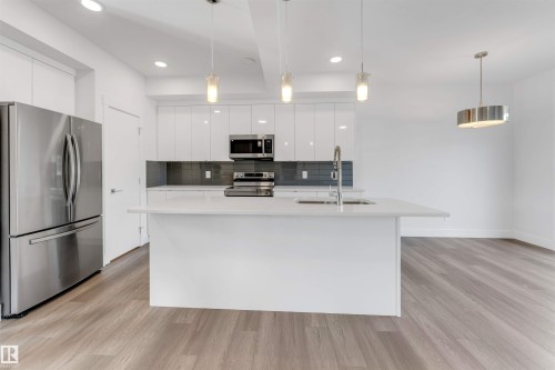 Modern kitchen featuring a white island with a sink, white cabinetry, stainless steel appliances, and a gray tiled backsplash