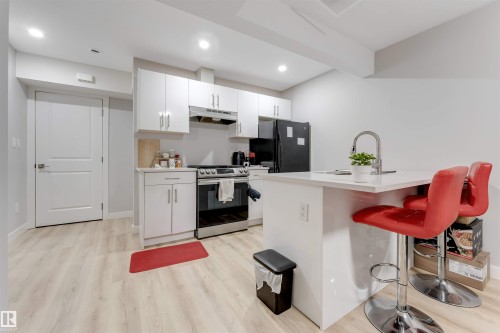 The kitchen features light wood-style flooring, white cabinetry, a stainless steel oven and range, and a kitchen island with a sink and seating