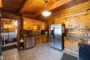 Kitchen featuring wood-paneled walls and ceiling, exposed wood beams, stainless steel appliances, dark countertops, and custom wood cabinetry with decorative black hardware