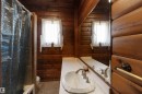 Bathroom featuring extensive wood paneling, a white countertop with an integrated sink, a large wall-mounted mirror, and a window with white sheer curtains
