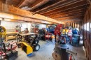 Spacious workshop area with exposed wood ceiling beams, concrete flooring, built-in shelving, a workbench, and a wood-burning stove
