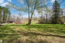 Expansive outdoor space featuring a large grassy area, mature trees, dense foliage, and a rustic outbuilding