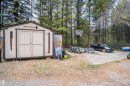 Outdoor shed with double doors, set on a gravel and concrete pad, surrounded by mature trees