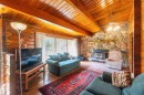 Vaulted wood-paneled ceilings with exposed beams, stone-faced fireplace with wood stove insert, full-height window overlooking exterior scenery, natural wood walls, and wood-finish flooring