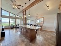 Open-concept living area featuring a vaulted ceiling with exposed beam, expansive windows, wood-finish flooring, and a large kitchen island with a stone countertop