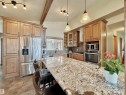Kitchen featuring a large granite-style island, stainless steel appliances, wood cabinetry, vaulted ceiling with track lighting, and a mosaic tile backsplash