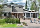 Rear exterior featuring a sunroom addition with multiple windows, a wood pergola, and a stone veneer foundation
