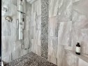 Walk-in shower featuring a pebble tile floor, large format tile walls, and a multi-function shower panel