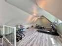Attic space featuring wood-finish flooring, track lighting, and a white railing with glass panels