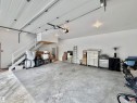 Spacious garage featuring a concrete floor, overhead garage door, built-in staircase, and an elevated storage platform