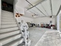 Spacious garage featuring a concrete floor, overhead garage door, built-in staircase with railing, white painted walls, and an exposed electrical panel