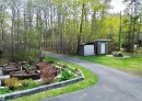 Paved driveway with bordering raised garden beds, a storage shed, and an additional outbuilding