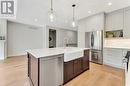 Kitchen with appliances with stainless steel finishes, an island with sink, sink, hanging light fixtures, and light wood-type flooring