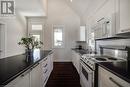 Kitchen with white appliances, a sink, dark countertops, white cabinets, and vaulted ceiling