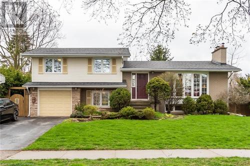 Split level home featuring driveway, a chimney, a front yard, a garage, and stone siding