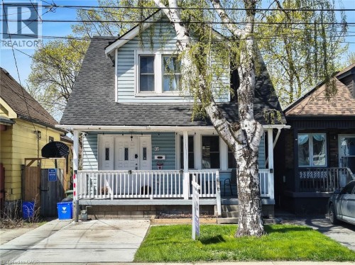 Light blue siding exterior featuring a covered porch with white railing, double entry doors, a gray asphalt shingle roof, and a mature tree in the front yard