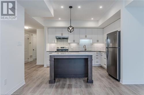 Kitchen with decorative light fixtures, light wood-type flooring, white cabinetry, and stainless steel appliances